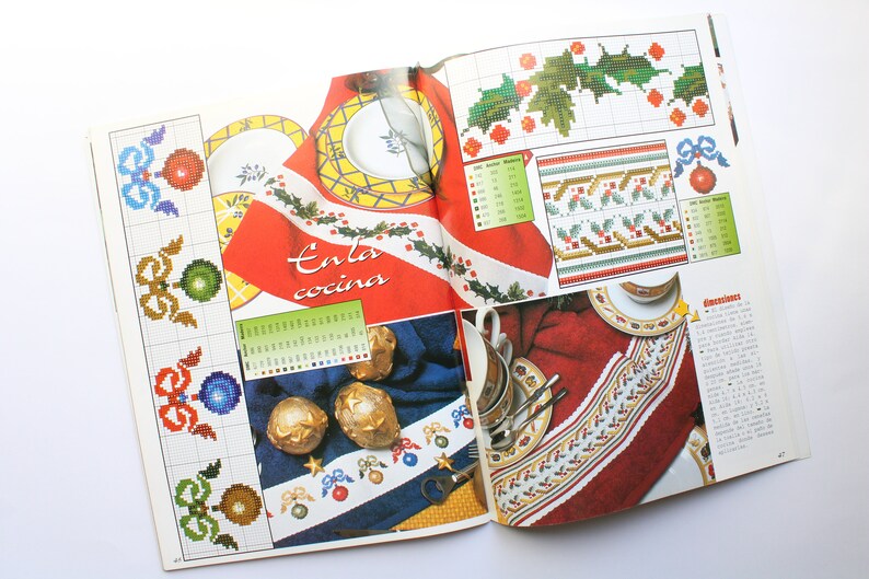 May include: A magazine page with cross-stitch patterns for holiday decorations. The patterns include holly leaves, bows, and ornaments. The text on the page reads "En la cocina".