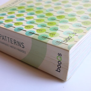 Puede incluir: Un libro verde y azul con un patrón de hojas y círculos. El libro se titula "Patterns" y tiene la palabra "booos" impresa en la portada.