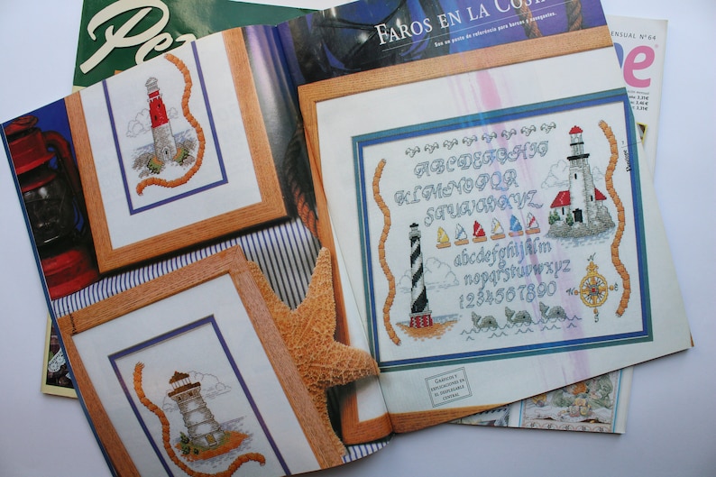 May include: A magazine page with three cross-stitch patterns featuring lighthouses and nautical themes. The patterns include an alphabet, numbers, and a lighthouse with a rope design. The magazine page is titled "Faros en la Costa".