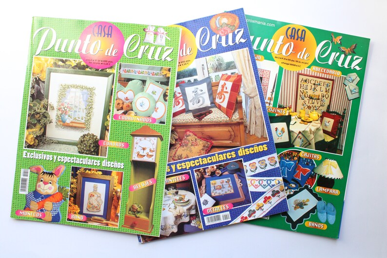 May include: Three colorful magazines with the title "Casa Punto de Cruz" on the cover. Each magazine features cross-stitch patterns and projects, including pillows, cushions, and a clock.