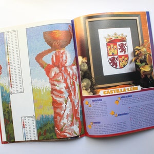 May include: A magazine page with a colorful cross-stitch pattern of a woman carrying a basket on her head. The page also includes a cross-stitch pattern of a coat of arms with the text "CASTILLA-LEON".