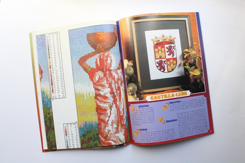 May include: A magazine page with a colorful cross-stitch pattern of a woman carrying a basket on her head. The page also includes a cross-stitch pattern of a coat of arms with the text "CASTILLA-LEON".