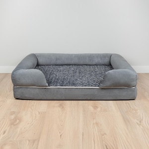 May include: A grey dog bed with a plush, textured surface and a raised rim. The bed has white piping around the edge.