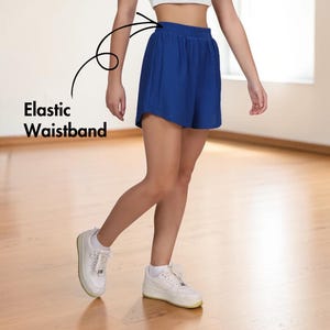 May include: Royal blue shorts with an elastic waistband. The shorts are paired with white sneakers. The text "Elastic Waistband" is visible in the image.