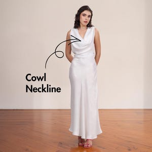 May include: A sleeveless, floor-length white satin dress with a cowl neckline. The dress has a simple, elegant design and is worn by a person. The text "Cowl Neckline" is next to the dress.