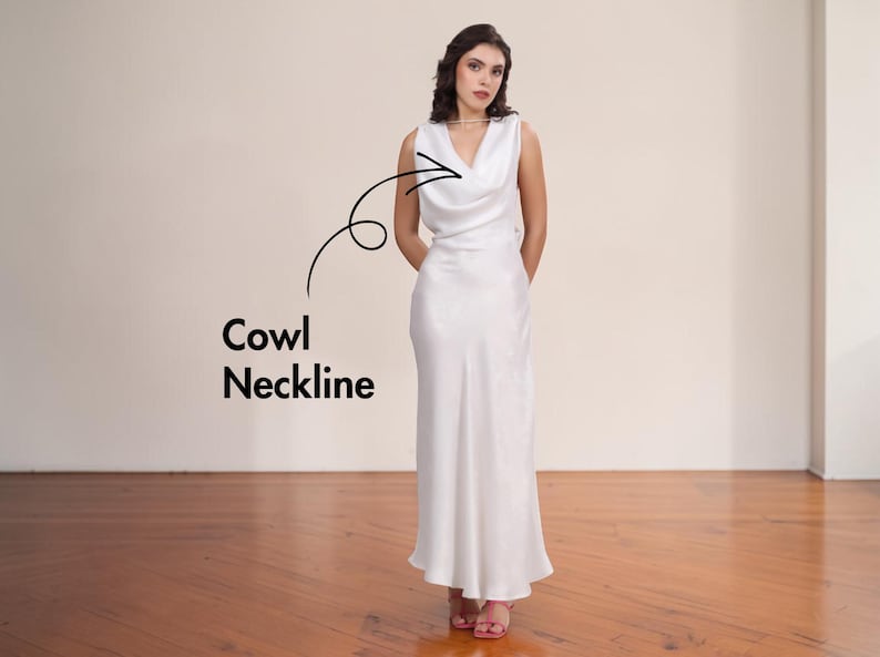 May include: A sleeveless, floor-length white satin dress with a cowl neckline. The dress has a simple, elegant design and is worn by a person. The text "Cowl Neckline" is next to the dress.
