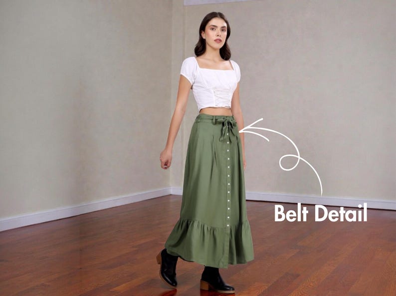 Op de afbeelding: Een vrouw draagt een witte crop top met vierkante hals en een olijfgroene maxi rok. De rok heeft een knoopsluiting aan de voorkant, een strikceintuur en een gefranjerde zoom. Zwarte enkellaarsjes maken de outfit compleet.