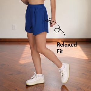 May include: Royal blue shorts with a relaxed fit. The shorts are paired with white sneakers. The text "Relaxed Fit" is next to the shorts. The shorts are made of a lightweight material.