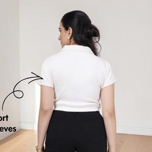 May include: A white polo shirt with a collar and short sleeves, featuring a black hand-drawn arrow pointing to the left sleeve with the text Short Sleeves written in black below the arrow, paired with black pants.