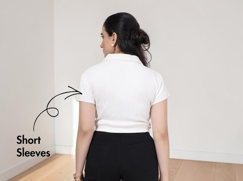 May include: A white polo shirt with a collar and short sleeves, featuring a black hand-drawn arrow pointing to the left sleeve with the text Short Sleeves written in black below the arrow, paired with black pants.