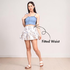 May include: A light blue denim crop top with tie straps paired with a white floral print mini skirt. The skirt has a fitted waist and a flared design. The outfit is completed with white sandals.