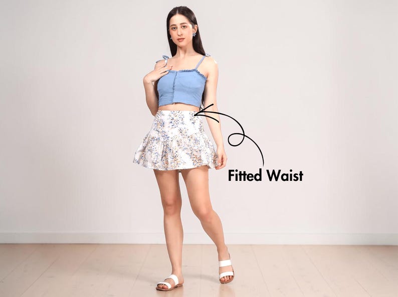 May include: A light blue denim crop top with tie straps paired with a white floral print mini skirt. The skirt has a fitted waist and a flared design. The outfit is completed with white sandals.