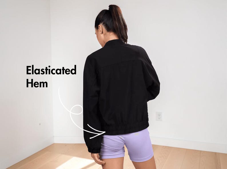 Pode incluir: &Eacute; apresentada uma jaqueta preta com bainha el&aacute;stica. A modelo est&aacute; usando shorts lil&aacute;s. O texto "Bainha el&aacute;stica" &eacute; exibido no lado esquerdo da imagem.