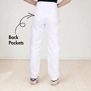 May include: White cargo pants featuring a high-waisted design, straight legs, and two large back pockets. A black arrow points to the back pockets with the text "Back Pockets" written in black next to the arrow, highlighting the pocket placement.