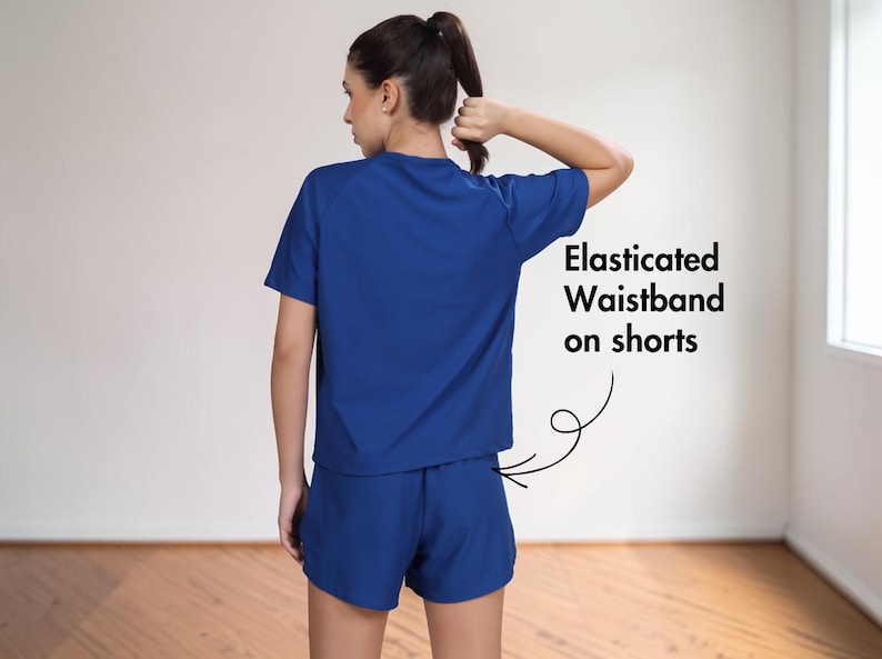 Puede incluir: Un conjunto deportivo azul, compuesto por una camiseta de manga corta y unos pantalones cortos. Los pantalones cortos tienen una cintura el&aacute;stica. El texto en la imagen dice: "Cintura el&aacute;stica en pantalones cortos".