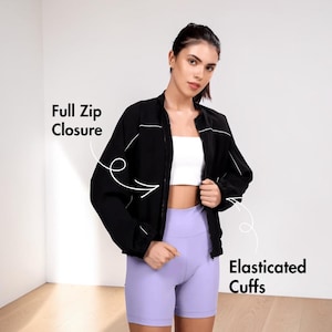 Pode incluir: Uma jaqueta preta com fecho de z&iacute;per completo e punhos el&aacute;sticos. A jaqueta &eacute; usada sobre um top branco e combinada com shorts lavanda. A imagem mostra as caracter&iacute;sticas da jaqueta.