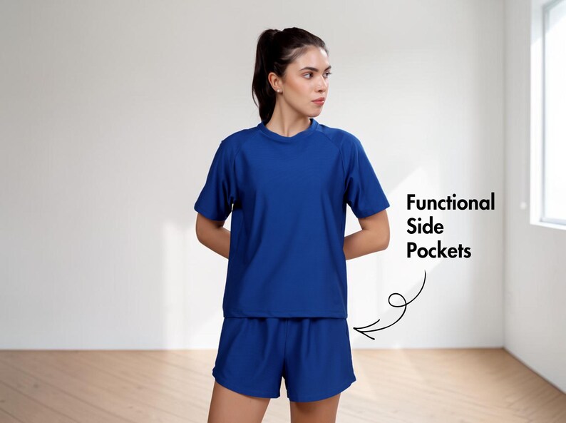 Puede incluir: Una mujer con un conjunto deportivo azul a juego de camiseta y pantal&oacute;n corto. La camiseta tiene mangas cortas y cuello redondo. El pantal&oacute;n corto tiene cintura el&aacute;stica. El texto en la imagen dice "Functional Side Pockets".