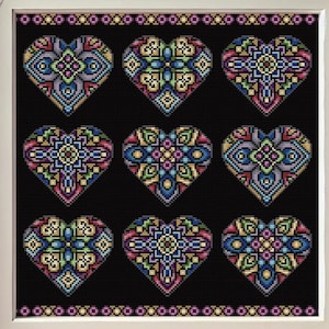Può includere: Uno schema di punto croce con nove cuori colorati con intricati disegni geometrici su uno sfondo nero. Lo schema è incorniciato in una cornice di legno chiaro.