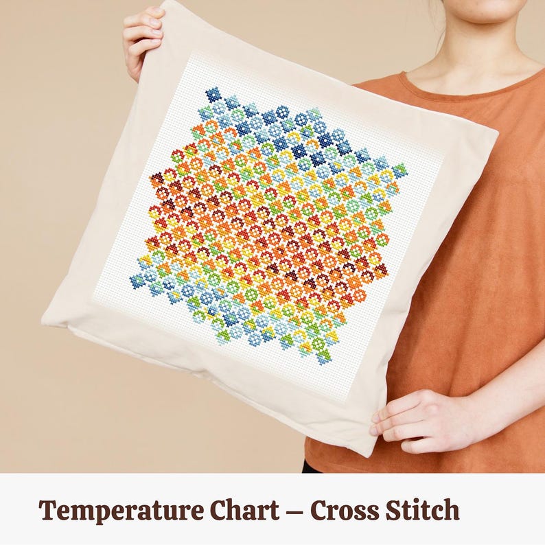 Op de afbeelding: Een vierkant, cr&egrave;mekleurig kussen met een kruissteekontwerp. Het kruissteekpatroon heeft een kleurrijk, geometrisch ontwerp in een verloop van blauw, groen, geel, oranje en rood. De tekst "Temperature Chart - Cross Stitch" staat onderaan.