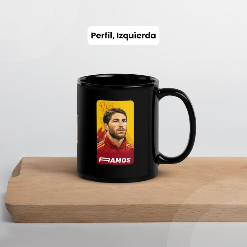 May include: A black ceramic mug with a portrait of a footballer in a red and yellow uniform. The mug has the text "RAMOS" and the number "15" on a yellow background. The text "Perfil, Izquierda" is above the mug.