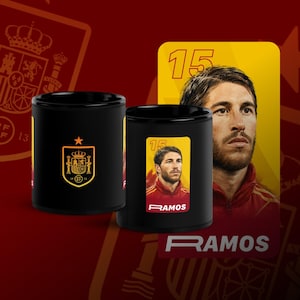 May include: Two black ceramic mugs featuring Spanish soccer player Sergio Ramos. One mug displays the Spanish coat of arms, while the other showcases a portrait of Ramos with the number 15. The word "RAMOS" is printed on the mug.