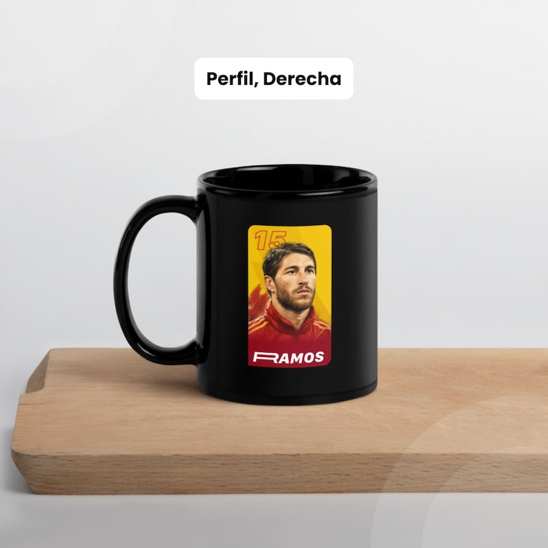 May include: Black ceramic mug with a portrait of a man in a red and yellow jersey. The mug has a large handle and a rectangular sticker with the number 15 and the name RAMOS.