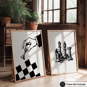 May include: Two framed art prints featuring chess-themed illustrations. One print shows a hand holding a chess piece above a checkered pattern. The other print displays various chess pieces. Both prints have a neutral color palette.