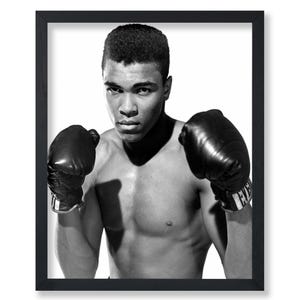 May include: Black and white photo of a boxer wearing boxing gloves. The boxer is shirtless and has a determined expression on his face.
