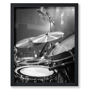 May include: Black and white photograph of a drum set with cymbals and microphones. The drums are in focus, with the cymbals and microphones slightly blurred in the background. The image is framed in a black border.