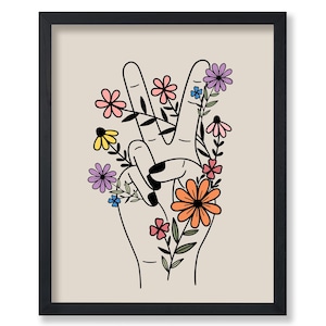 May include: A black framed print with a beige background featuring a hand making the peace sign with colorful flowers growing around the fingers.