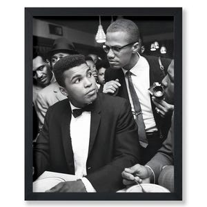 May include: Black and white framed photograph featuring Muhammad Ali and Malcolm X in a crowded room. Ali, in a suit and bow tie, looks to the side. Malcolm X, in a suit and tie, stands behind him. Other figures are visible in the background.