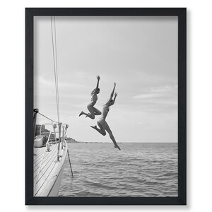 May include: Black and white framed print of two people jumping into the ocean from a sailboat. The image captures a moment of joy and freedom, with the subjects silhouetted against the sky and water. The sailboat's deck is visible in the foreground.