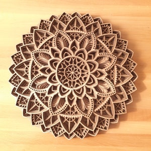 Op de afbeelding: Een houten mandala met ingewikkelde geometrische patronen en een gelaagd ontwerp. De mandala is gemaakt van meerdere lagen hout, waardoor een driedimensionaal effect ontstaat.