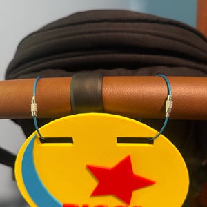 Peut inclure: Une &eacute;tiquette ovale jaune et bleue avec une &eacute;toile rouge et le texte "RIGGS FAMILY". L'&eacute;tiquette est fix&eacute;e &agrave; une poign&eacute;e marron avec une sangle noire. L'&eacute;tiquette est fix&eacute;e avec un fil bleu.