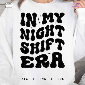 May include: White sweatshirt with black text that reads "In My Night Shift Era" in a retro font. The text is surrounded by small stars.