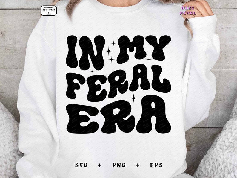 May include: White sweatshirt with black text that reads "In My Feral Era" in a retro font. The text is surrounded by small stars.