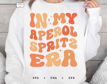 May include: White sweatshirt with the text "In My Aperol Spritz Era" in orange and peach retro font.