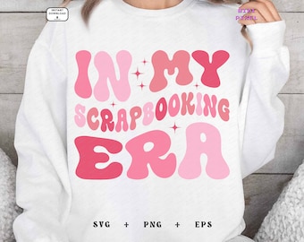 Può includere: Felpa bianca con scritta rosa "In My Scrapbooking Era". Le lettere sono in un font retrò e bombato.
