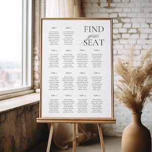 May include: A white seating chart with black text lists guest names and table numbers for a wedding reception. The chart is titled "Find Your Seat" and is displayed on a wooden easel.