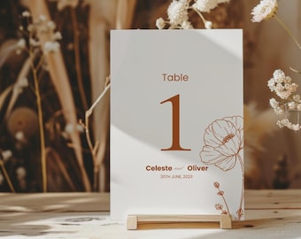 May include: White table number card with a brown floral design and the text "Table 1 Celeste and Oliver 30th June 2023".