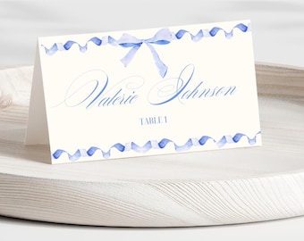 May include: Blue watercolor ribbon place card with a bow and the text "Valerie Johnson" and "Table 1".
