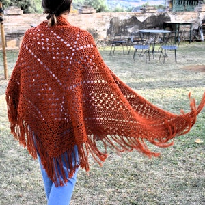 Könnte beinhalten: Ein rostiger Häkel-Schal mit Fransen. Der Schal ist über die Schultern einer Person gelegt und weht im Wind.