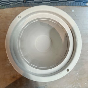 Top-down view of a white plaster mold cylinder with interior steps and small holes. Blue and white checkered fabric in the background.