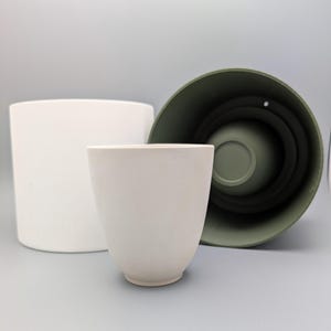 May include: Three white ceramic plant pots of different sizes. The largest pot is a cylinder, the medium pot is a cylinder, and the smallest pot is a rounded shape.