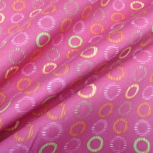 May include: Pink fabric with a repeating pattern of orange and green circles. The circles are outlined in white and have a striped pattern.
