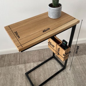 May include: A black metal side table with a wooden top and a small storage compartment. The table measures 46 cm wide, 25 cm deep, and 66 cm high. The storage compartment is 16 cm wide, 25 cm deep, and 6.5 cm high.