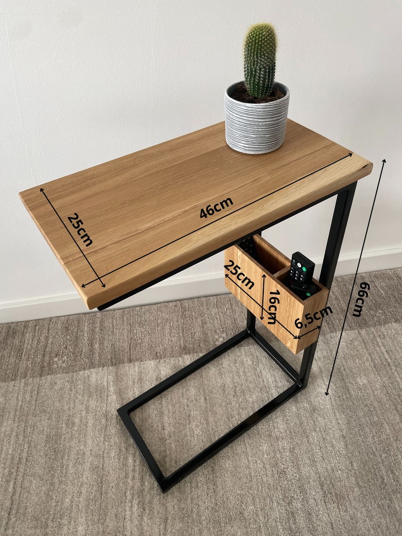 May include: A black metal side table with a wooden top and a small storage compartment. The table measures 46 cm wide, 25 cm deep, and 66 cm high. The storage compartment is 16 cm wide, 25 cm deep, and 6.5 cm high.