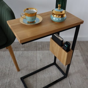 May include: A wooden side table with a black metal frame. The table has a shelf for storage and a small wooden box on the side. There is a cup and saucer, a sugar bowl, and a vase on the table.