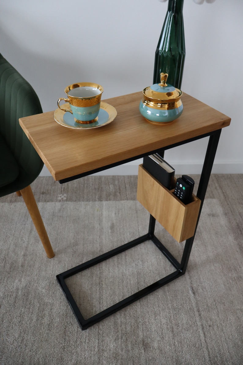 May include: A wooden side table with a black metal frame. The table has a shelf for storage and a small wooden box on the side. There is a cup and saucer, a sugar bowl, and a vase on the table.