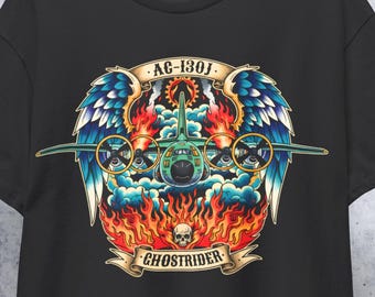 Puede incluir: Camiseta negra con un gráfico detallado de un avión militar con alas, hélices y llamas. El diseño incluye el texto "AC-130J" y "GHOSTRIDER" en una pancarta, con una calavera en la parte inferior. La camiseta está colgada en una percha de madera.